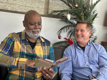 Man gifting ThinOptics Readers to another man, who is wearing them and reading a book.